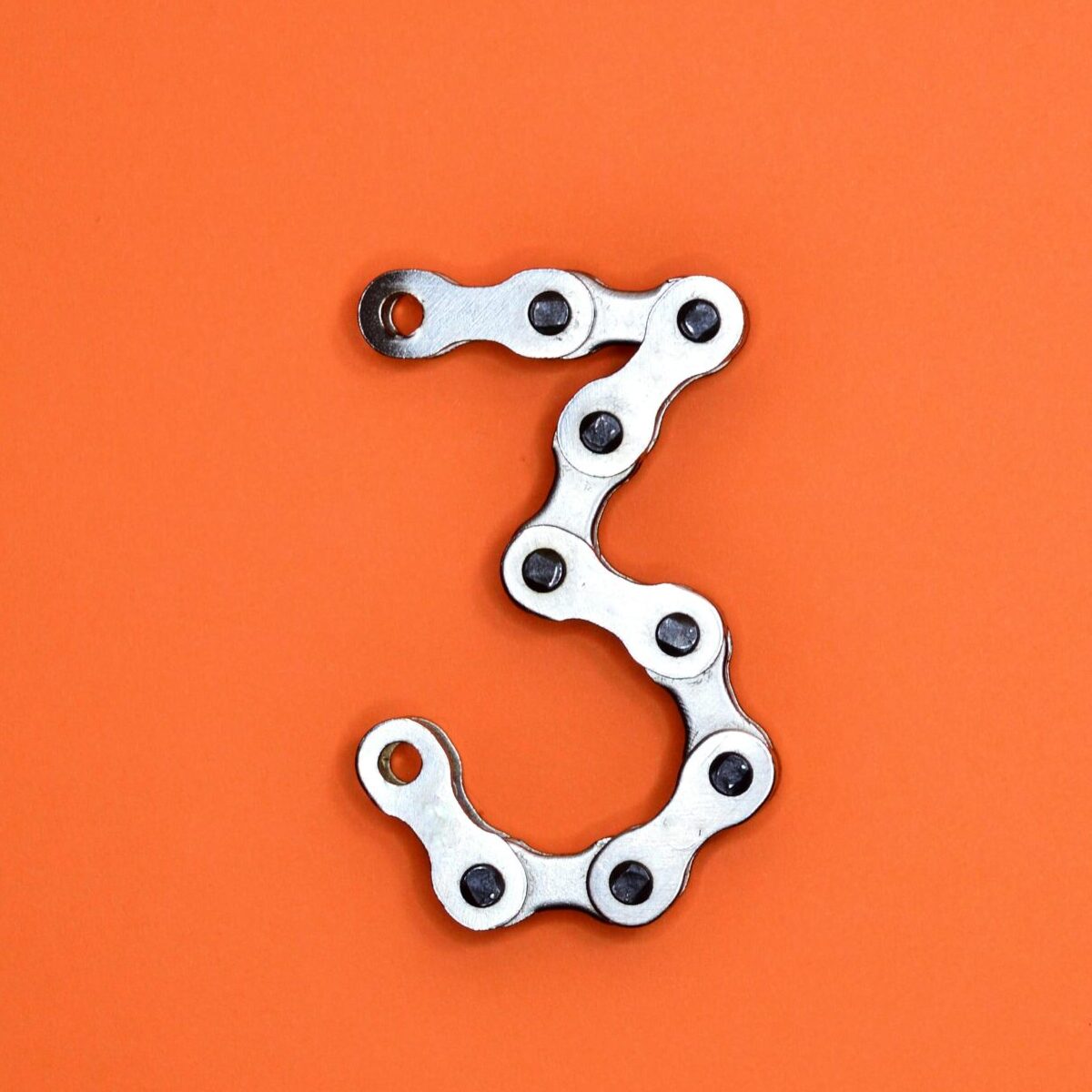 A bicycle chain forms the number three against a vibrant orange backdrop, offering ample copyspace.