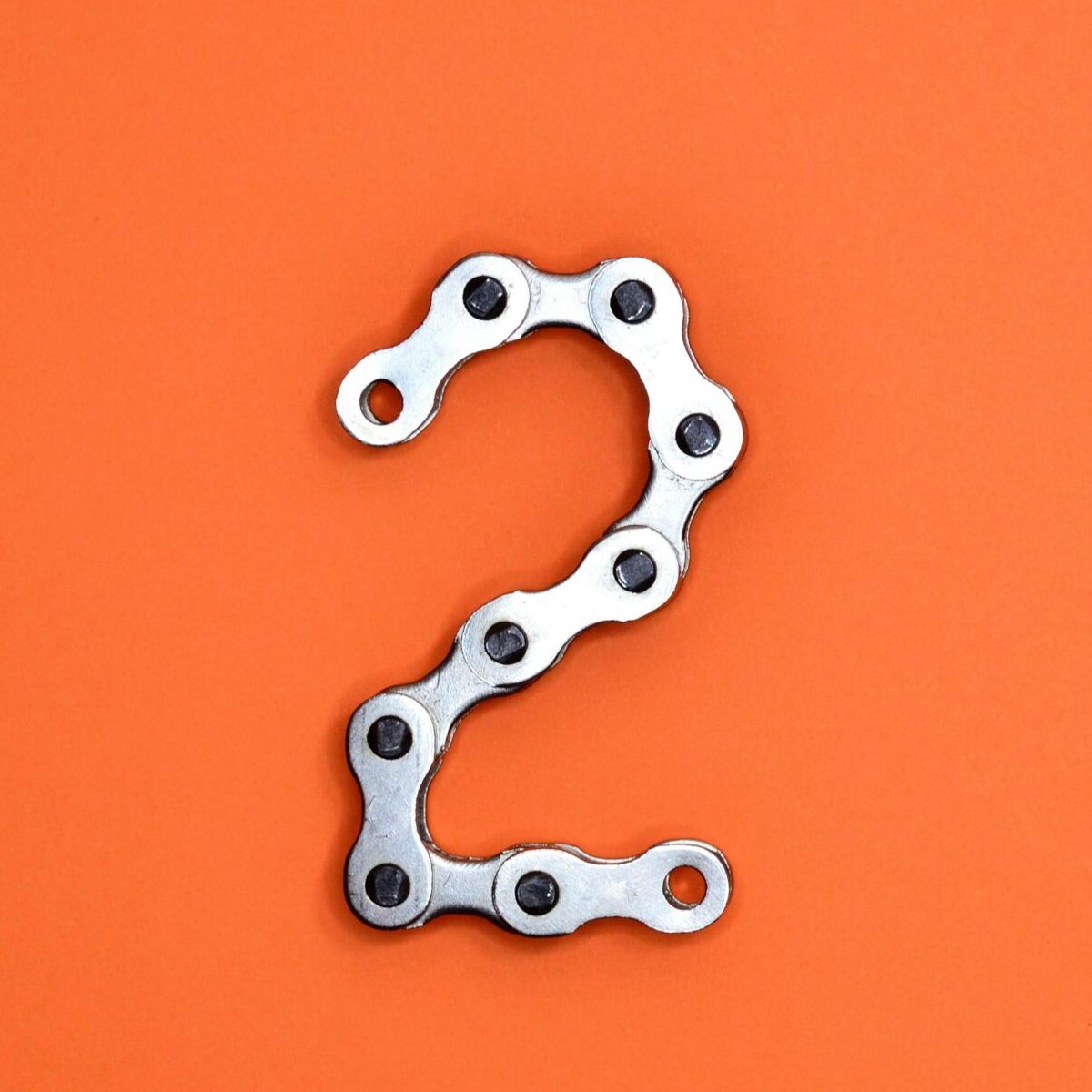 Metal chain forming the number 2 on a bright orange background, perfect for design projects.
