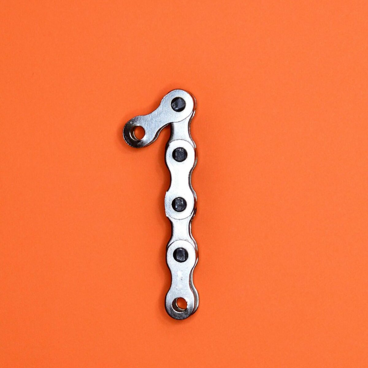 Metal chain forming the number one on an orange background, ideal for design concepts.